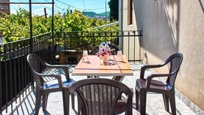 Un patio al aire libre con una mesa, dos sillas, un jarrón con flores y vistas a un viñedo.