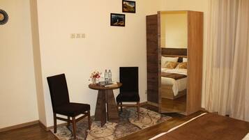 A hotel room with a bed, two chairs, a small table with a vase and bottles, and a mirror reflecting the bed.