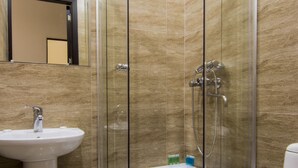 Un baño con ducha de vidrio, lavamanos pedestal y inodoro.