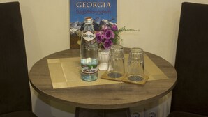Una mesa redonda de madera con una botella de agua mineral Borjomi, dos vasos de vidrio y un florero con flores moradas. En el fondo, un cartel de Georgia.