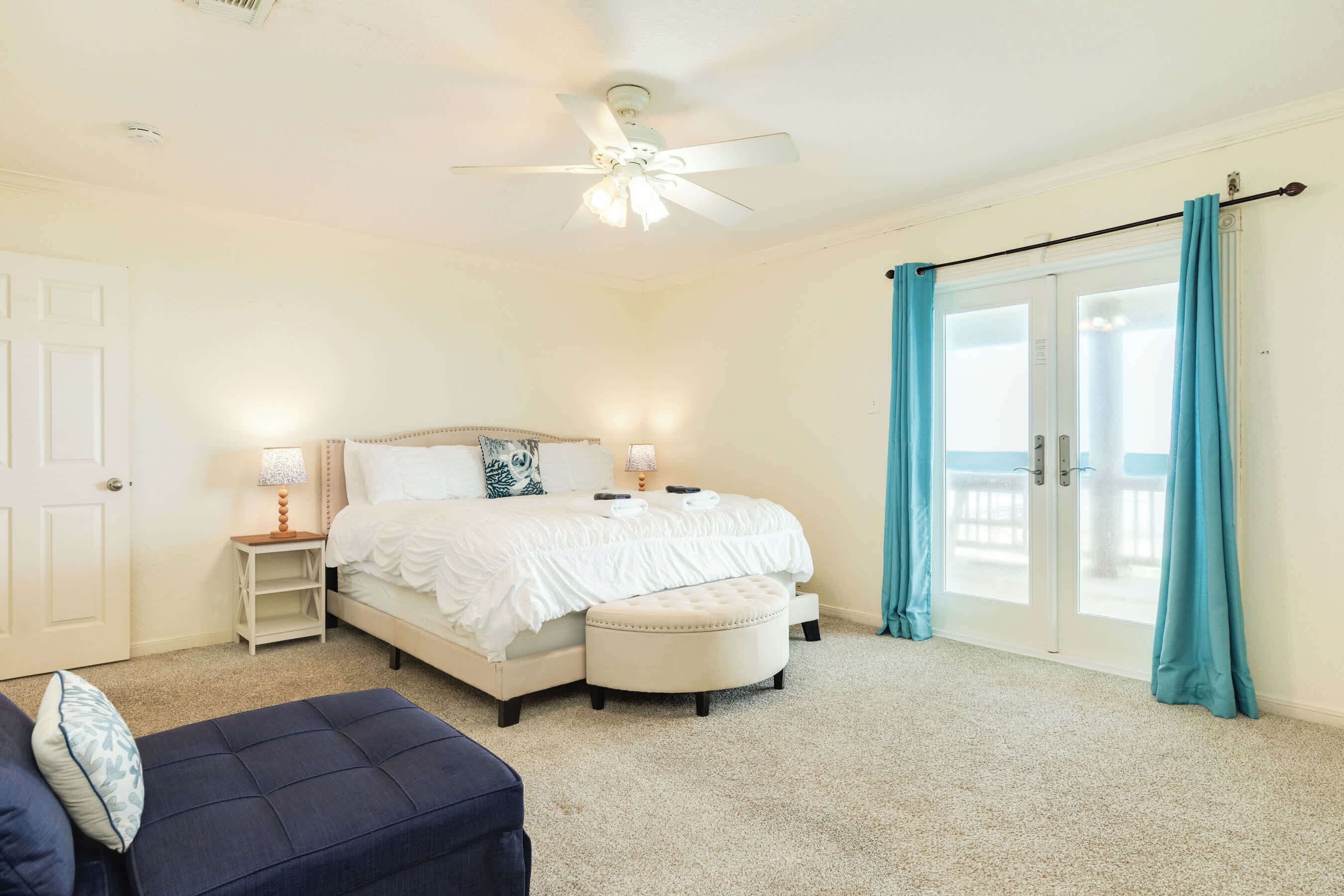 A bedroom with a bed, bedside tables, a ceiling fan, and a view through a sliding glass door.