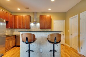 Una cocina con armarios de madera, una estufa de acero inoxidable, dos taburetes de bar y una puerta blanca.