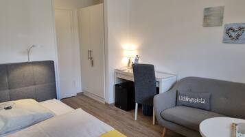 Ein Hotelzimmer mit einem Bett, einem Schreibtisch mit Lampe, einem grauen Sofa und einem kleinen runden Tisch.