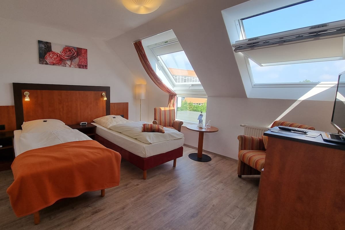 A hotel room with two beds, a desk, a chair, and a window with a view.