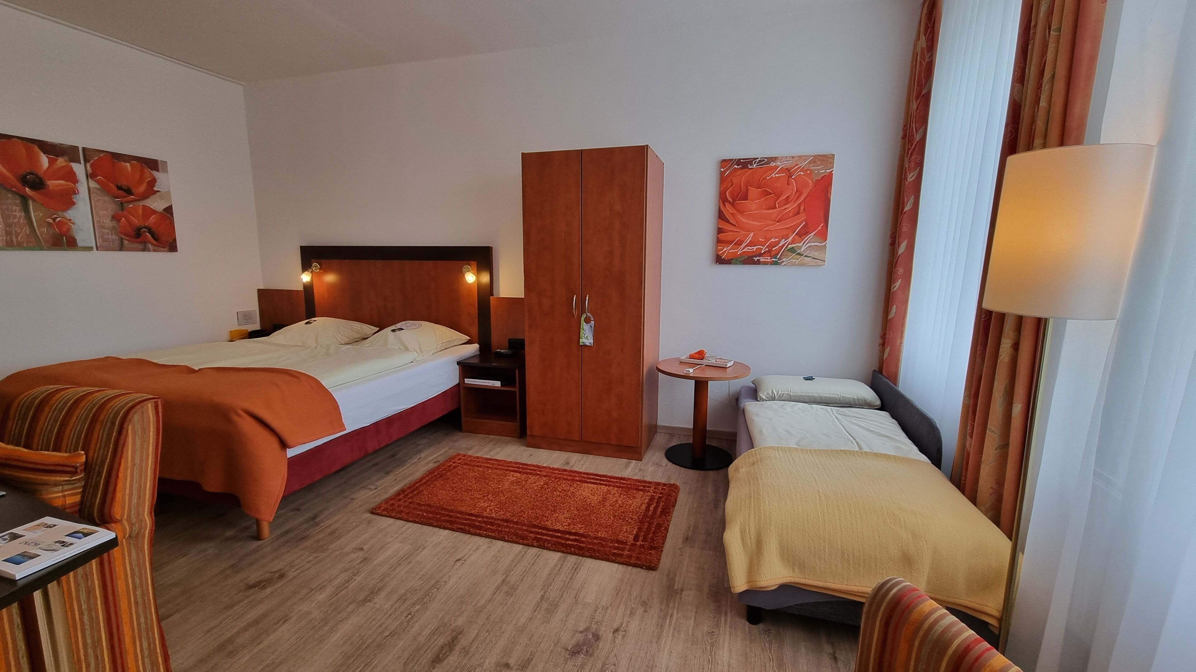 Ett hotellrum med två sängar, en garderob, ett litet bord och konstverk på väggarna.