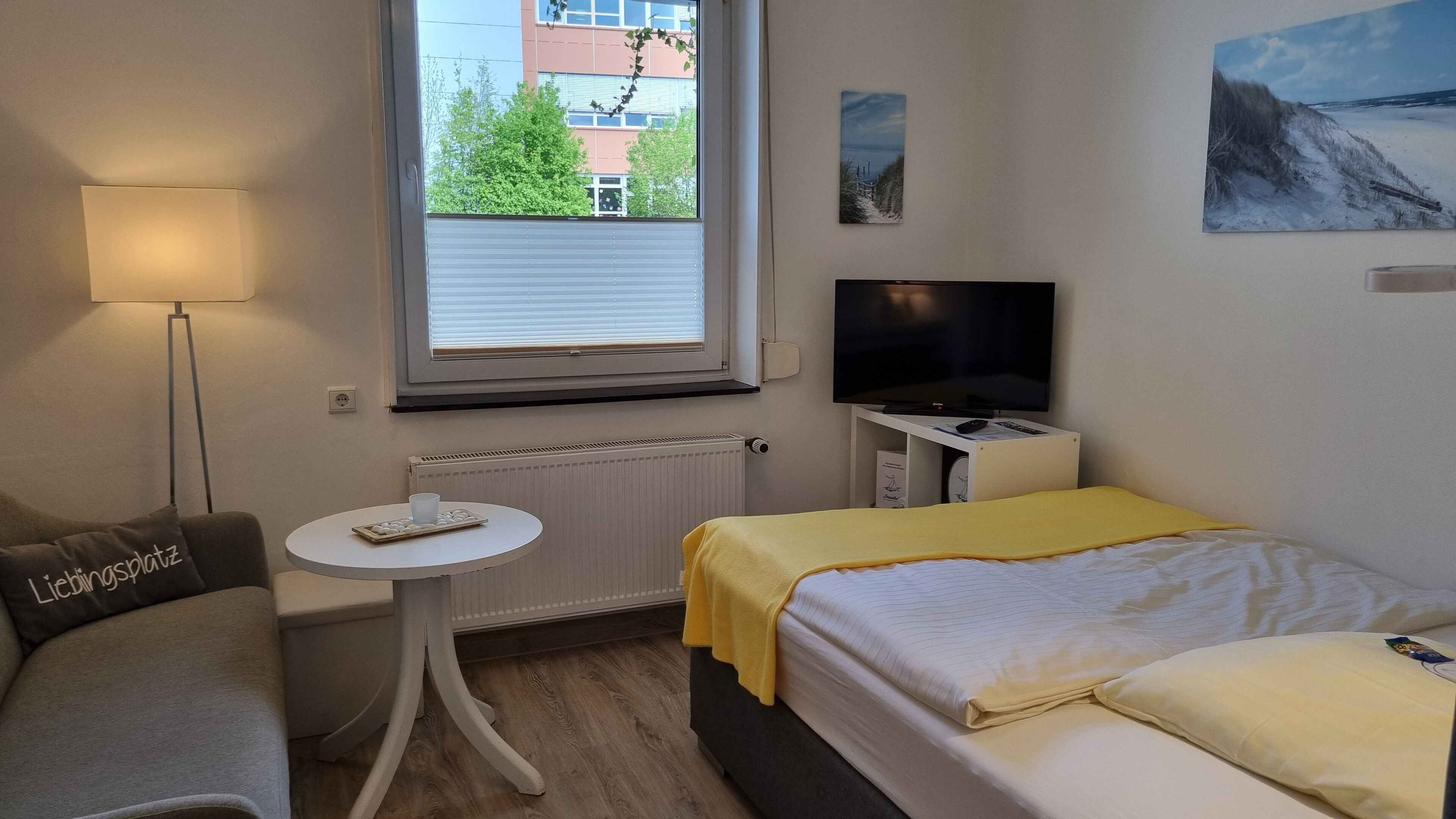 A hotel room with a bed, a small table with a tray of cookies, a lamp, a TV, and a painting on the wall.