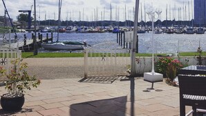 Een jachthaven met vele zeilboten afgemeerd, een vlag met tekst, en uitzicht op het water en de lucht.