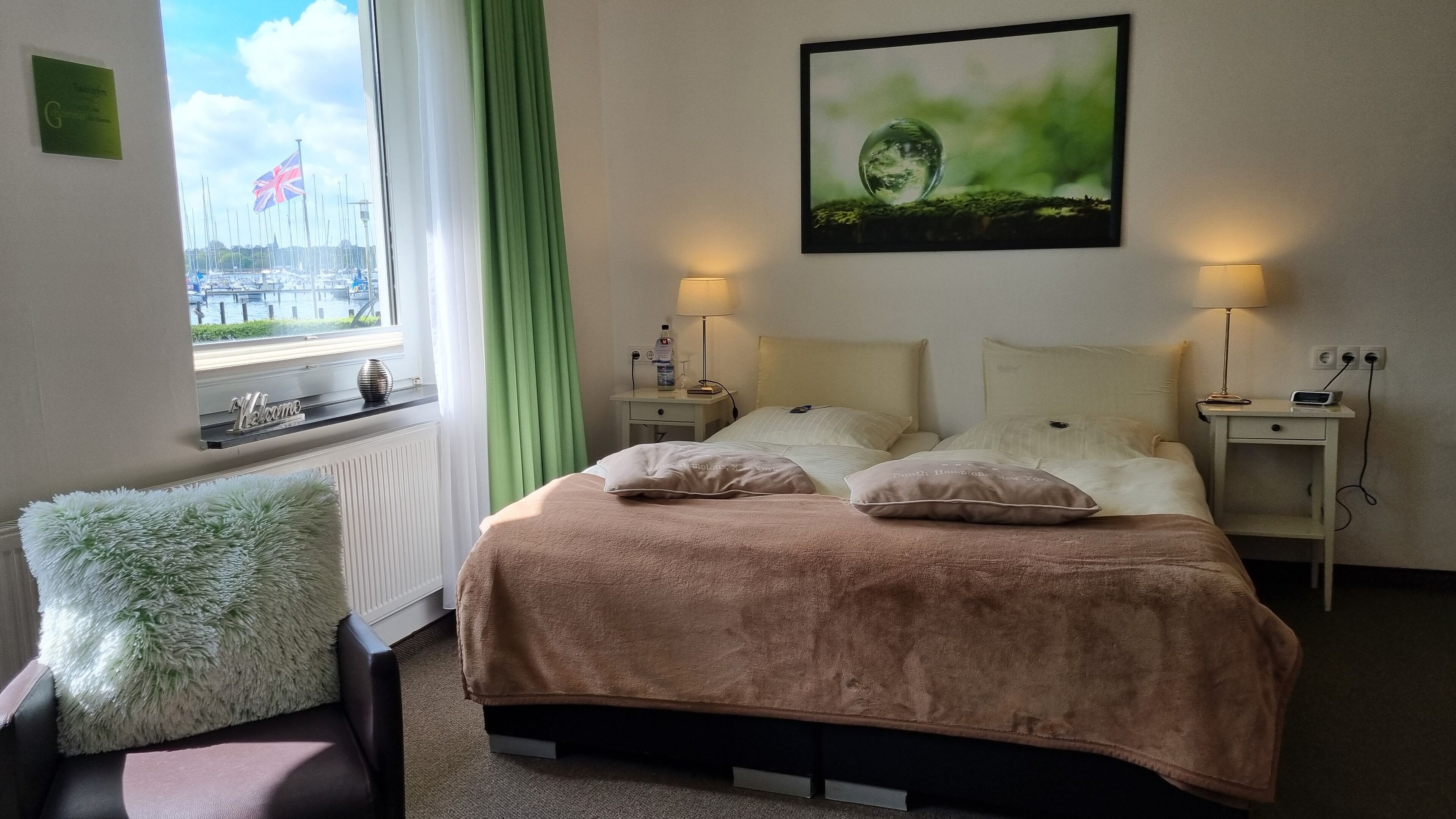 Et soveværelse med seng, to sengeborde, lampe, pude, stol, vindue med udsigt til både og et billede på væggen.