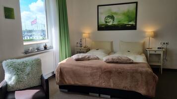 Et soveværelse med seng, to sengeborde, lampe, pude, stol, vindue med udsigt til både og et billede på væggen.