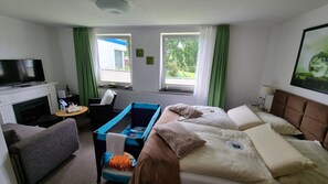Una habitación de hotel con cama, televisión, chimenea, ventana con cortinas y un cuadro en la pared.