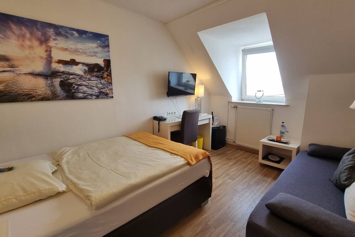 A compact room with a bed, a desk with a computer, a TV, and a couch.