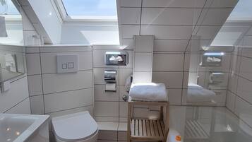 A compact, modern bathroom with a skylight, a toilet, a sink, and a small wooden shelf.
