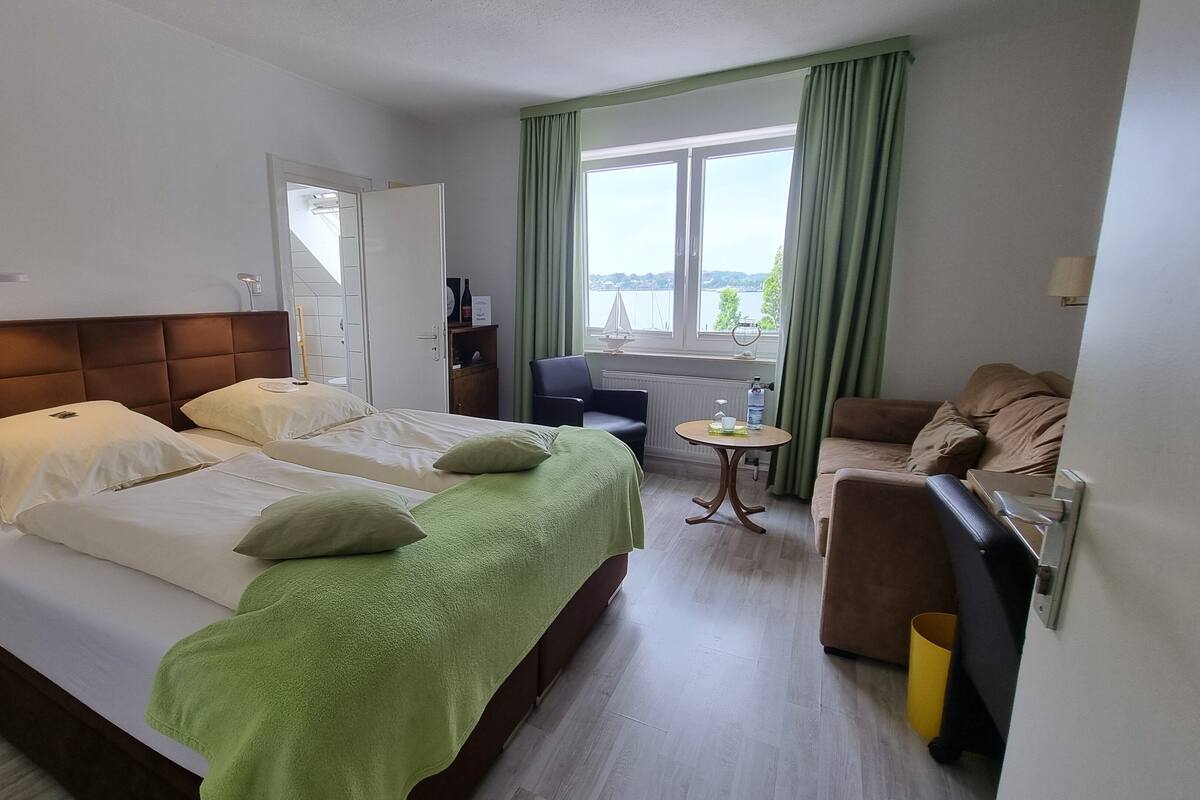 A hotel room with a large bed, a small table, a sofa, and a view of the outdoors.