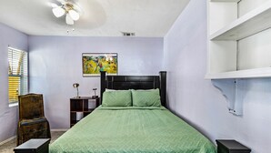 A bedroom with a bed, a chair, a nightstand, a painting, and a ceiling fan. - 1 bedroom Apartment in quaint triplex 12 blocks from UF and downtown (Gainesville)