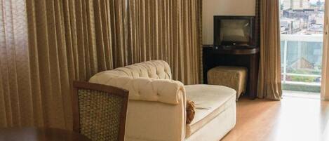 Habitación de hotel con sofá, televisión, una mesita y vistas a la ciudad a través de amplios ventanales.