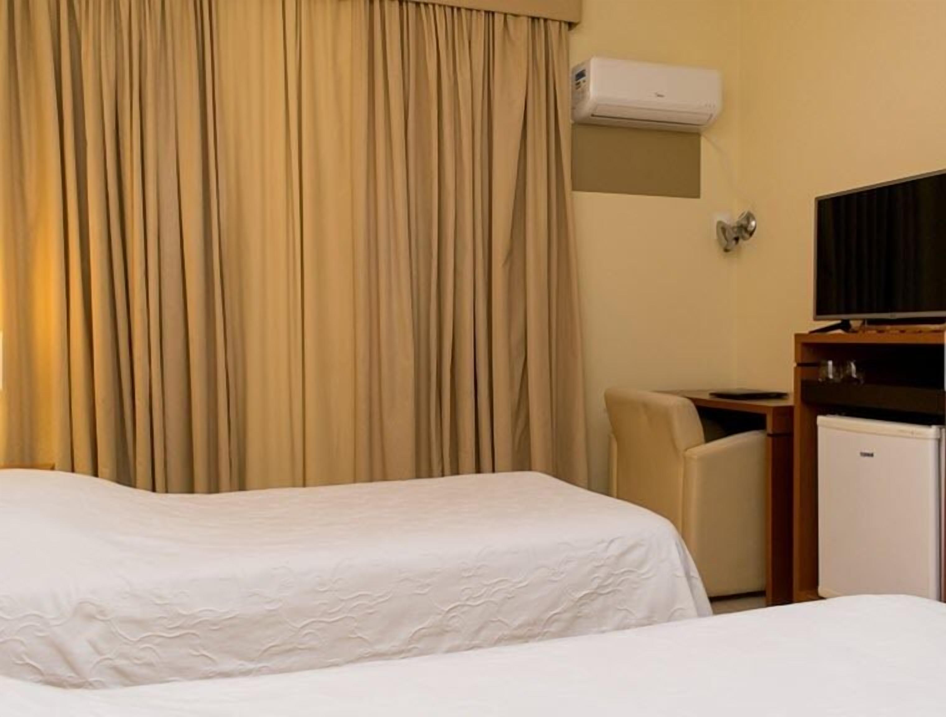Une chambre d’hôtel avec deux lits, un bureau, une chaise, un appareil de climatisation et un téléviseur.