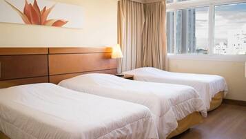 A hotel room with two single beds, a wooden headboard, a window with curtains, and a cityscape view.