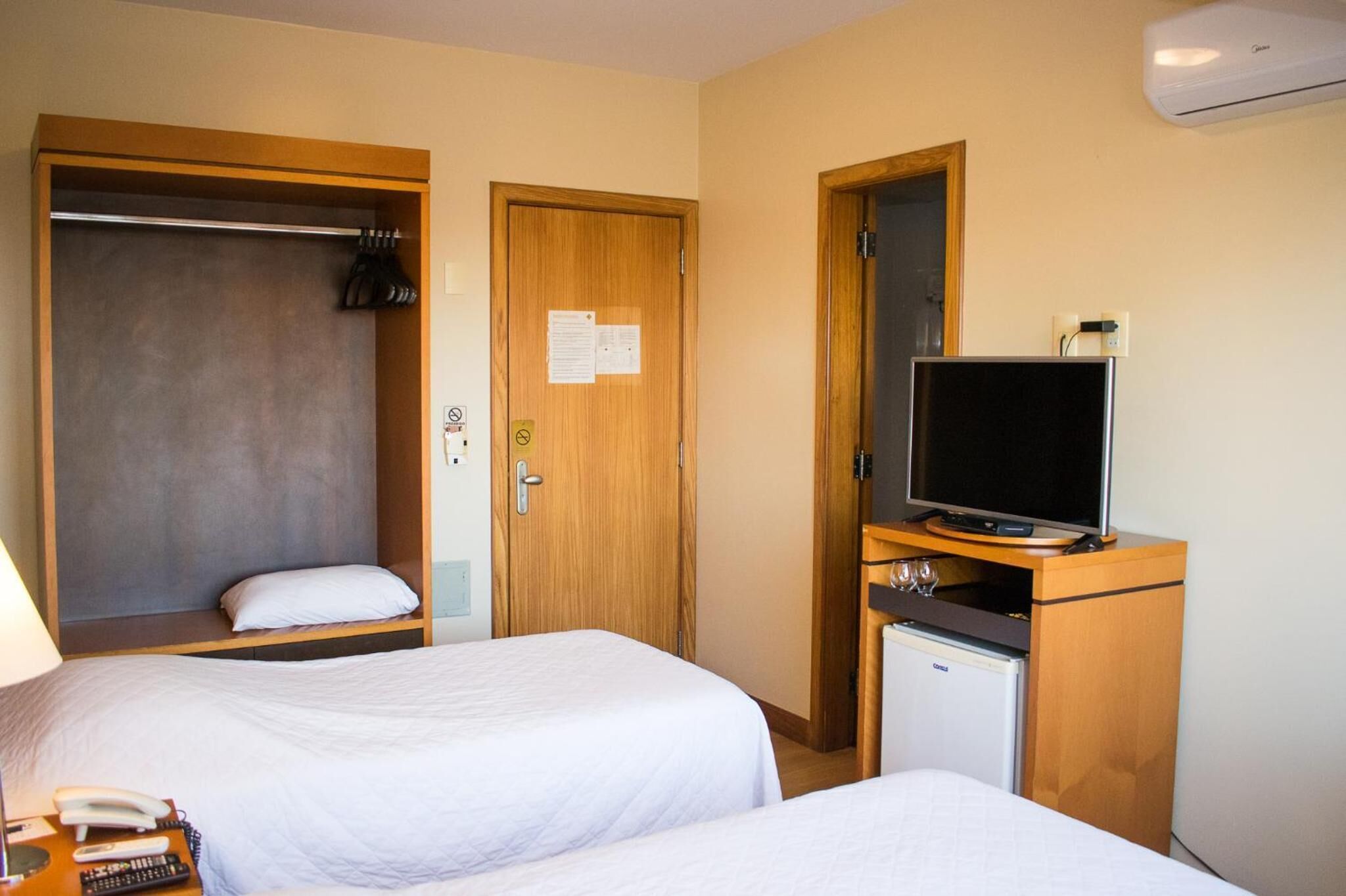 A hotel room with two beds, a wardrobe, a television, and a minibar.