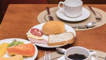 Una mesa con comida que incluye pan, queso, jamón y verduras, junto a una taza de café.