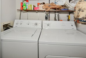 A laundry area with two front-loading washing machines and a shelf above containing cleaning supplies. - XPLORIE ACTIVITIES & LINENS INCLUDED*! QUAY 2 BR/2 BA Ocean View Condo with Indoor/Outdoor Pools. (Ocean City)