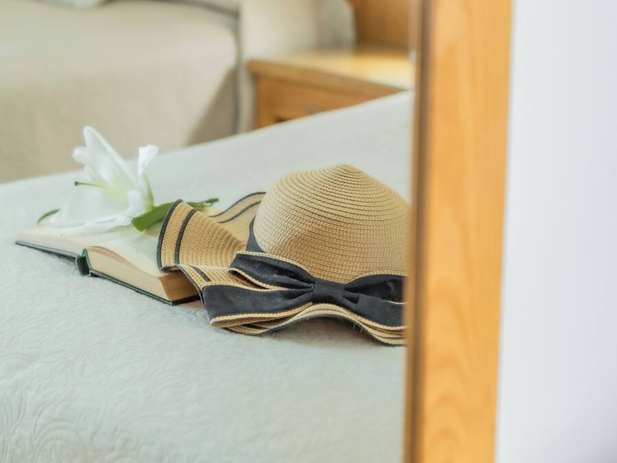 A neatly made bed with a white pillow, a book, and a straw hat.
