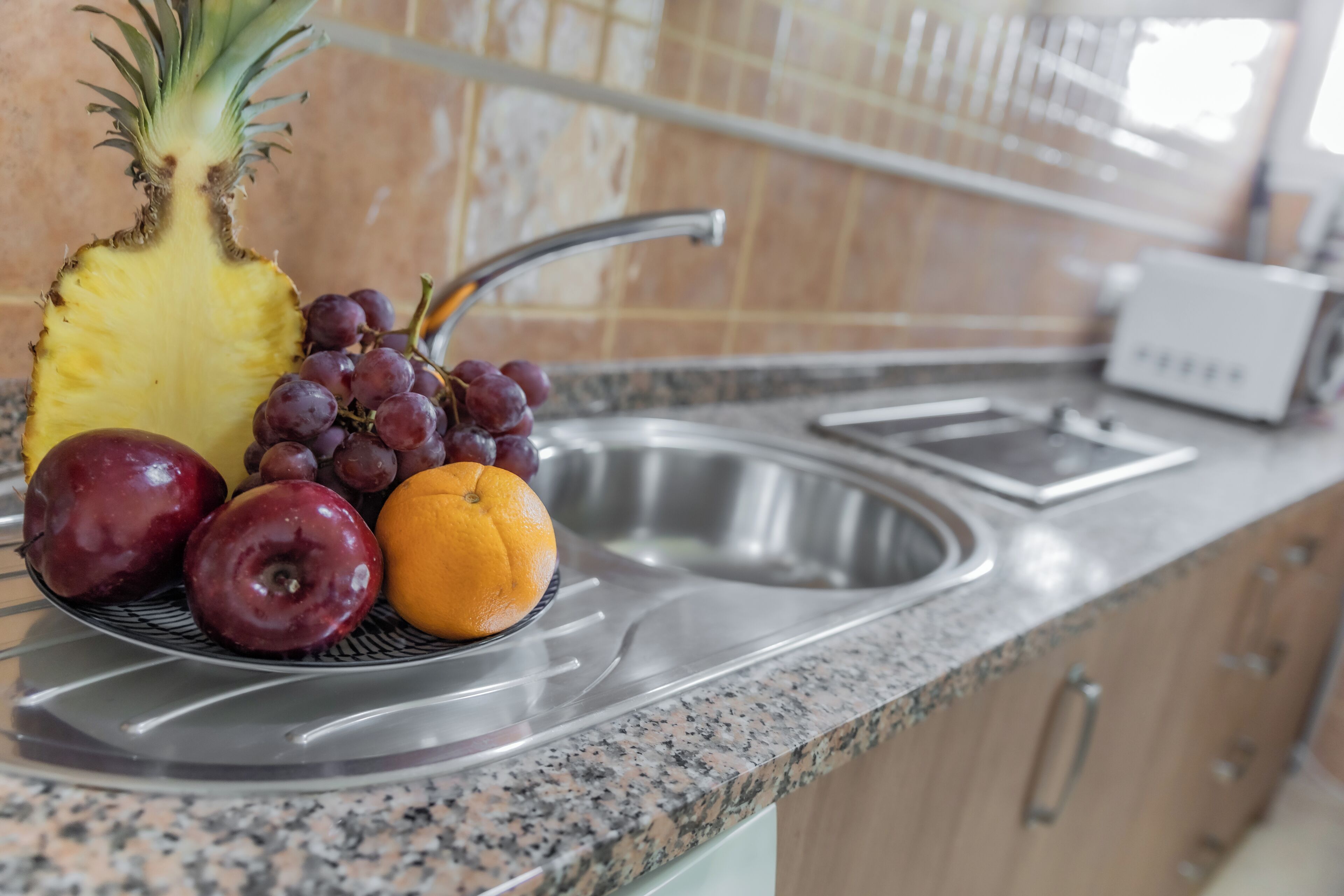 Una encimera de cocina con un frutero que contiene una piña, uvas, una manzana y una naranja.