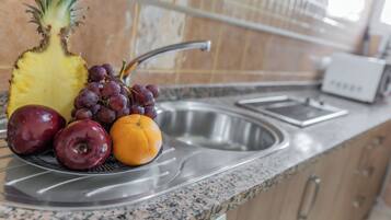 Una encimera de cocina con un frutero que contiene una piña, uvas, una manzana y una naranja.