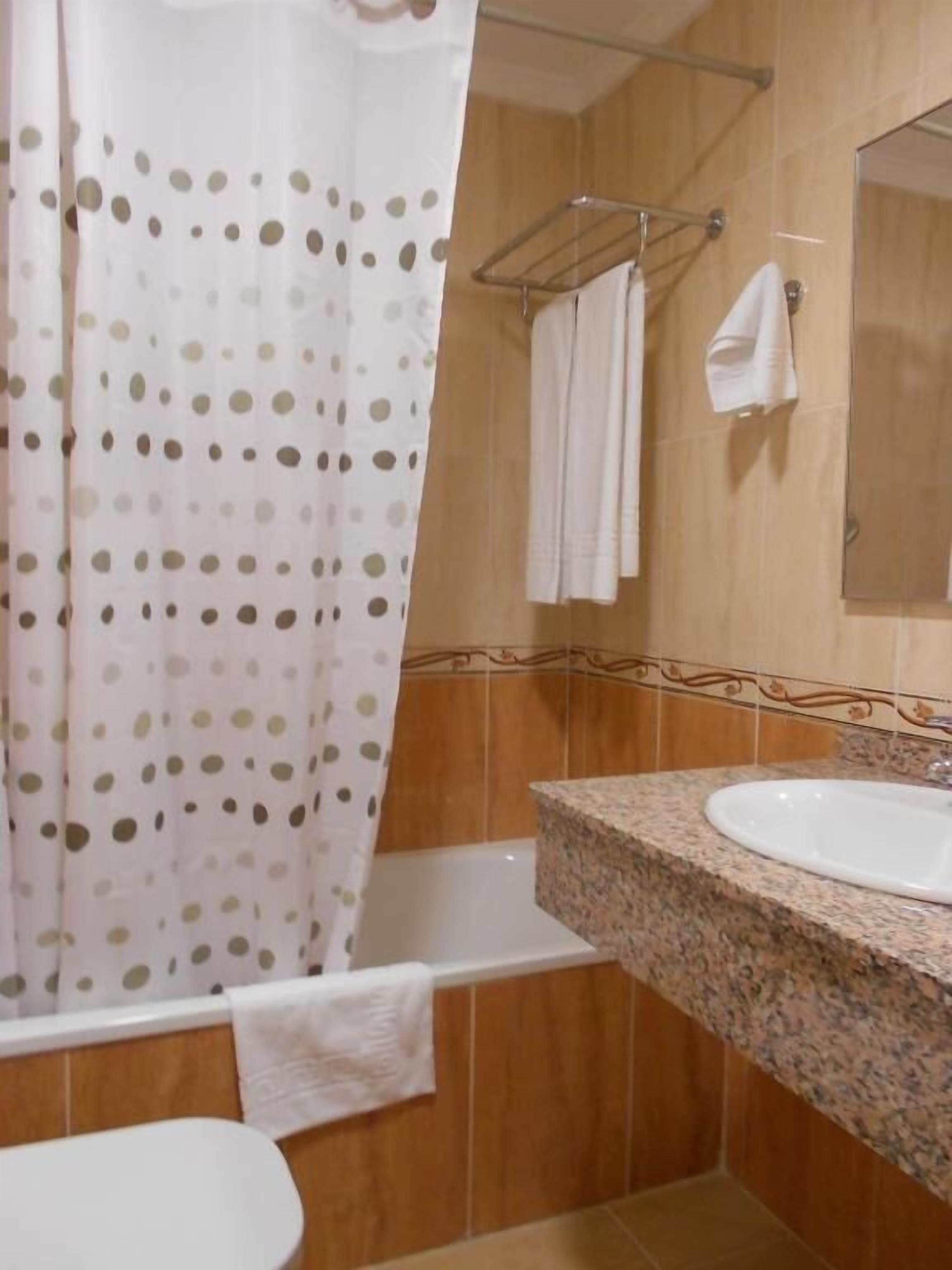 Un baño con inodoro blanco, lavamanos de granito, cortina de ducha con estampado de lunares y azulejos de madera.