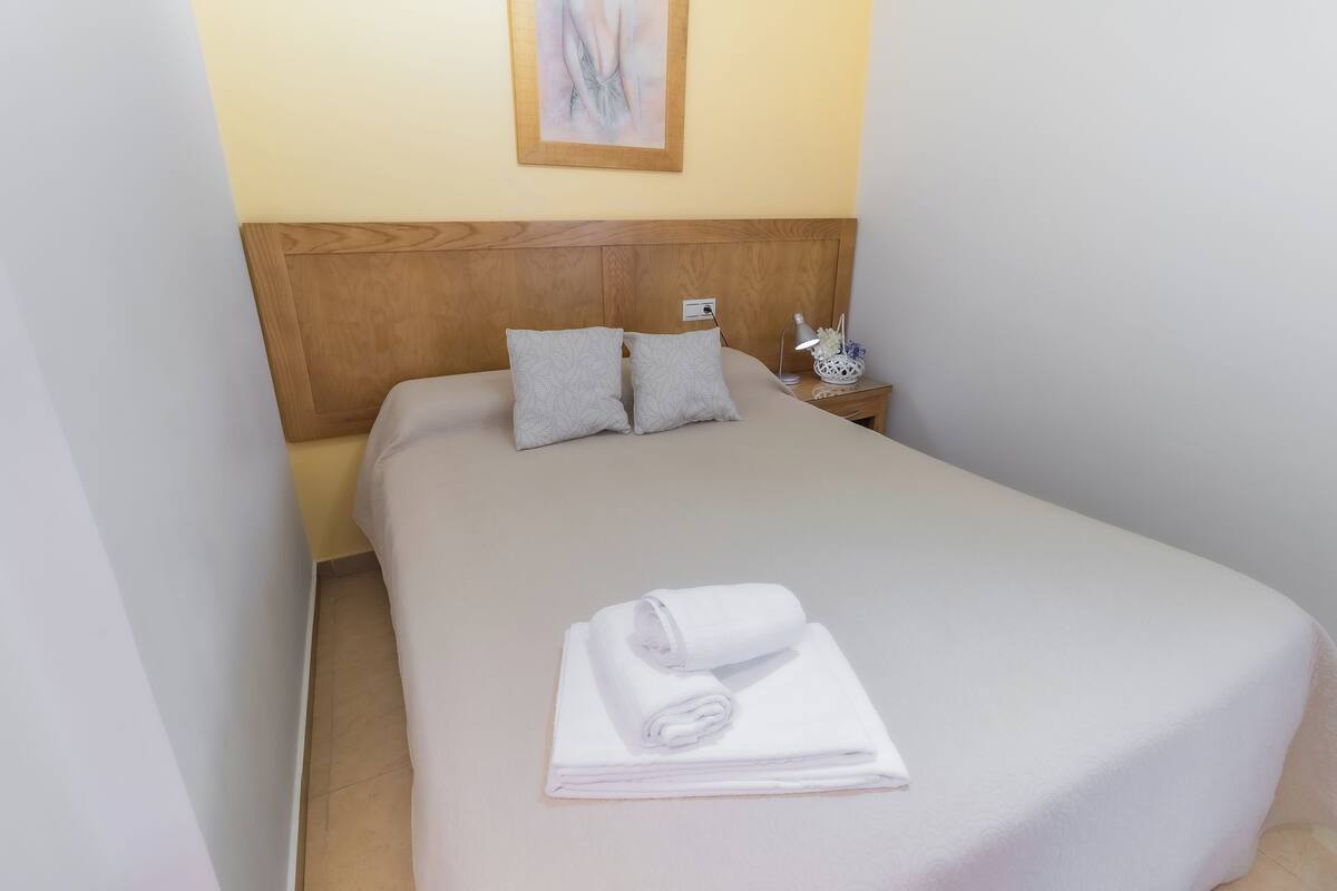 A neatly made bed with a wooden headboard, two pillows, and a folded towel on the bed.