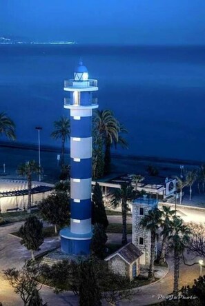 A lighthouse with a blue and white striped tower, surrounded by palm trees and a small building.