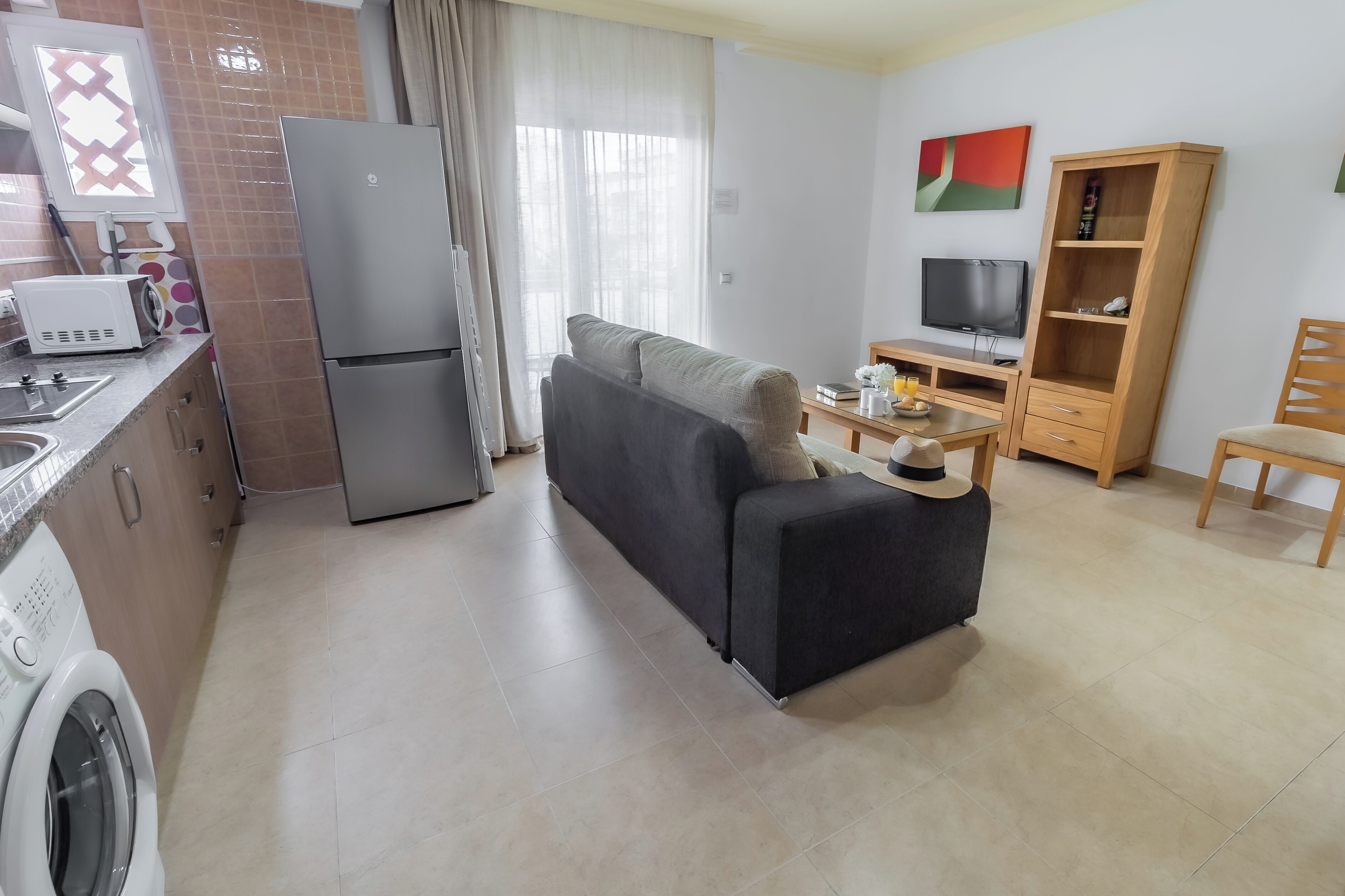 A compact living space with a kitchenette, a sofa, a television, and a wooden cabinet.
