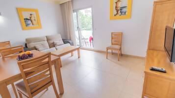 Una sala de estar con sofá, mesa de comedor con sillas, mueble para televisión y obras de arte en las paredes.