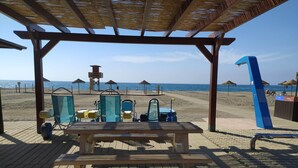 A beachside pavilion with a wooden table and chairs, a lifeguard tower, and beach umbrellas in the background. - Las Yucas  (Velez-Malaga)