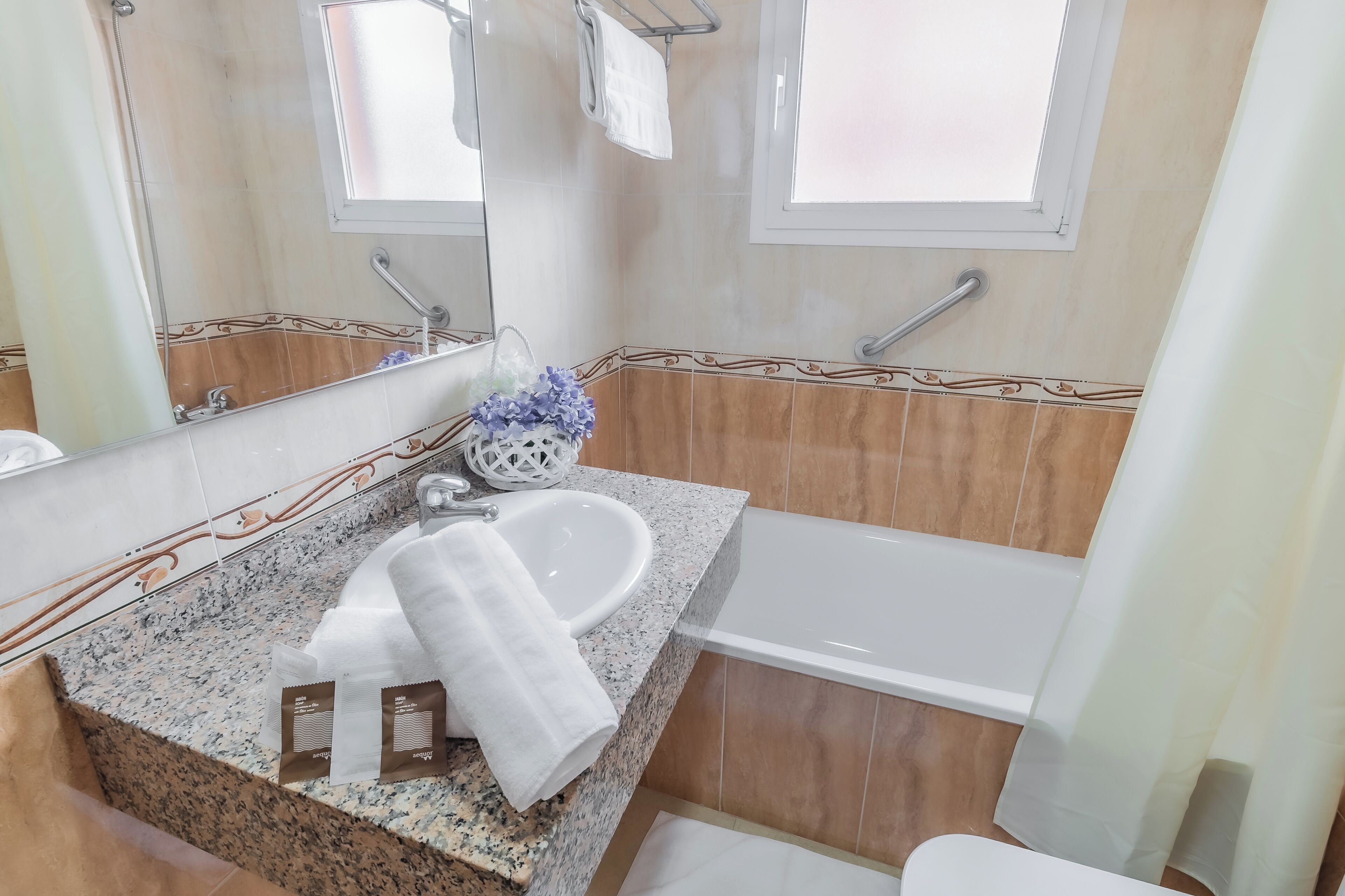 Un baño con encimera de granito, lavamanos blanco, espejo y bañera.