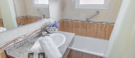 A bathroom with a granite countertop, a white sink, a mirror, and a bathtub.