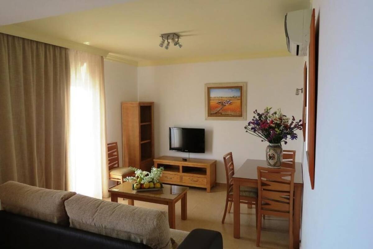 A living room with a sofa, TV, wooden cabinet, dining table, and chairs.