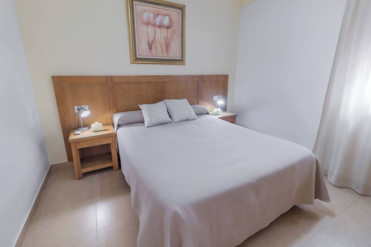 A neatly made bed with a wooden headboard, two bedside tables with lamps, and a framed artwork on the wall.