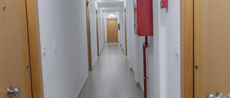 A long, narrow hallway with wooden doors on both sides, white walls, and a tiled floor.