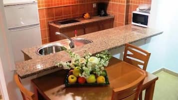 Een kleine keuken met een granieten aanrecht, een spoelbak en houten kastjes.