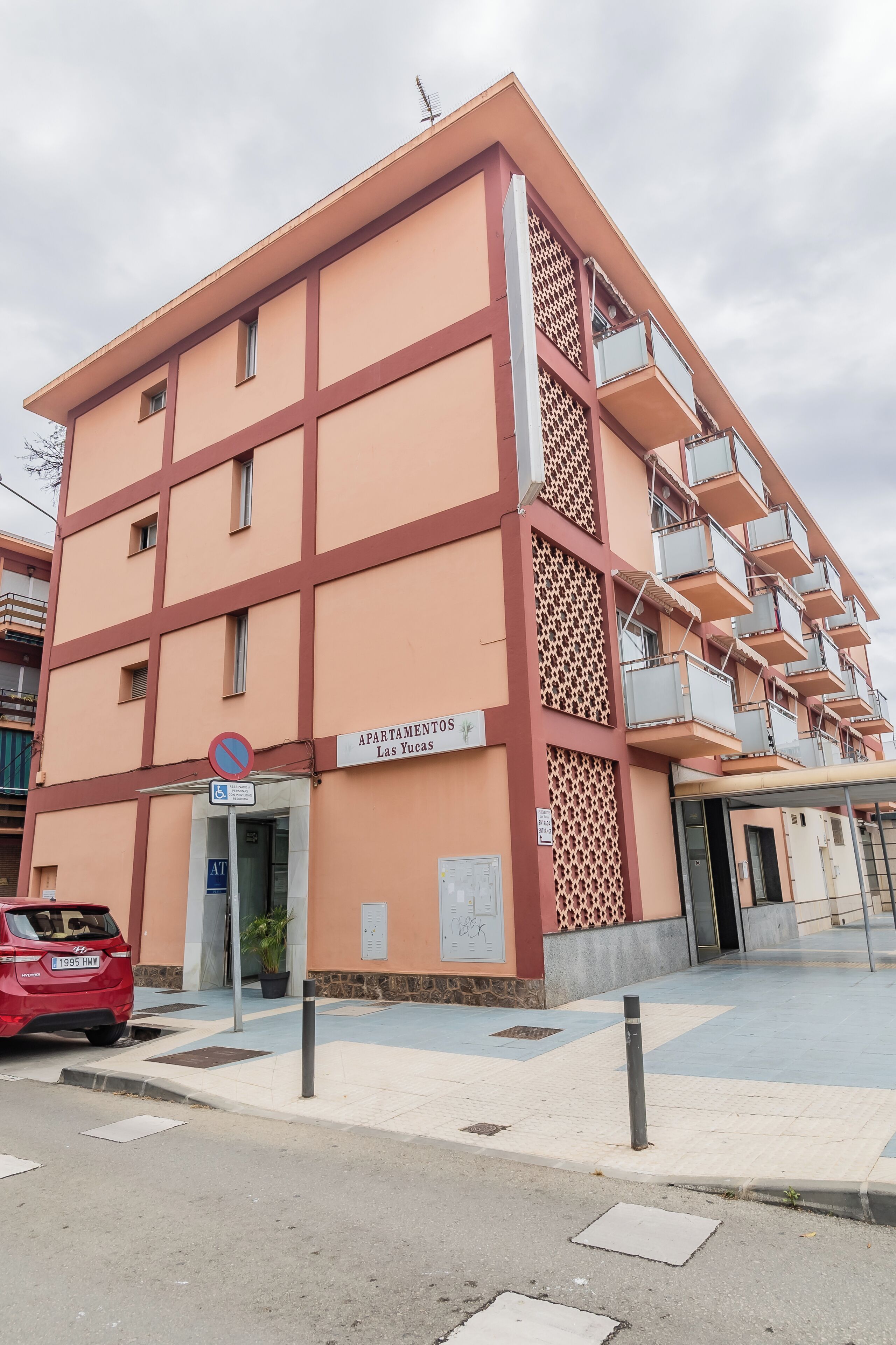 Een meerhoog gebouw met een bord waarop staat dat het een appartementencomplex is, genaamd 'Apartamentos Las Yucas'.
