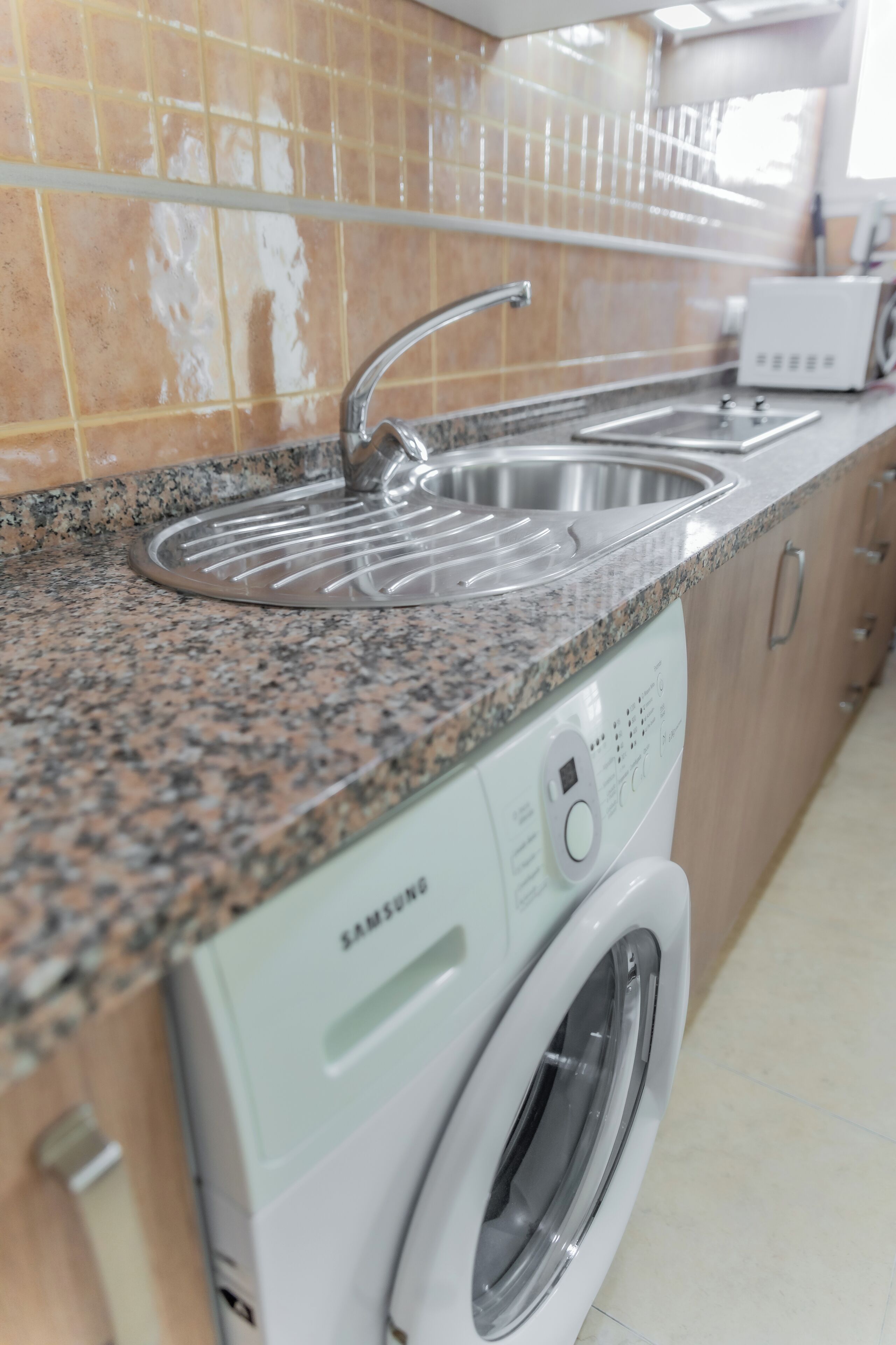 Une cuisine dotée d’un plan de travail en granit, d’un évier en acier inoxydable et d’un lave-linge Samsung à chargement frontal.