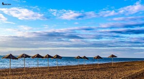 Ein Strand mit Reetdachschirmen und blauem Himmel.