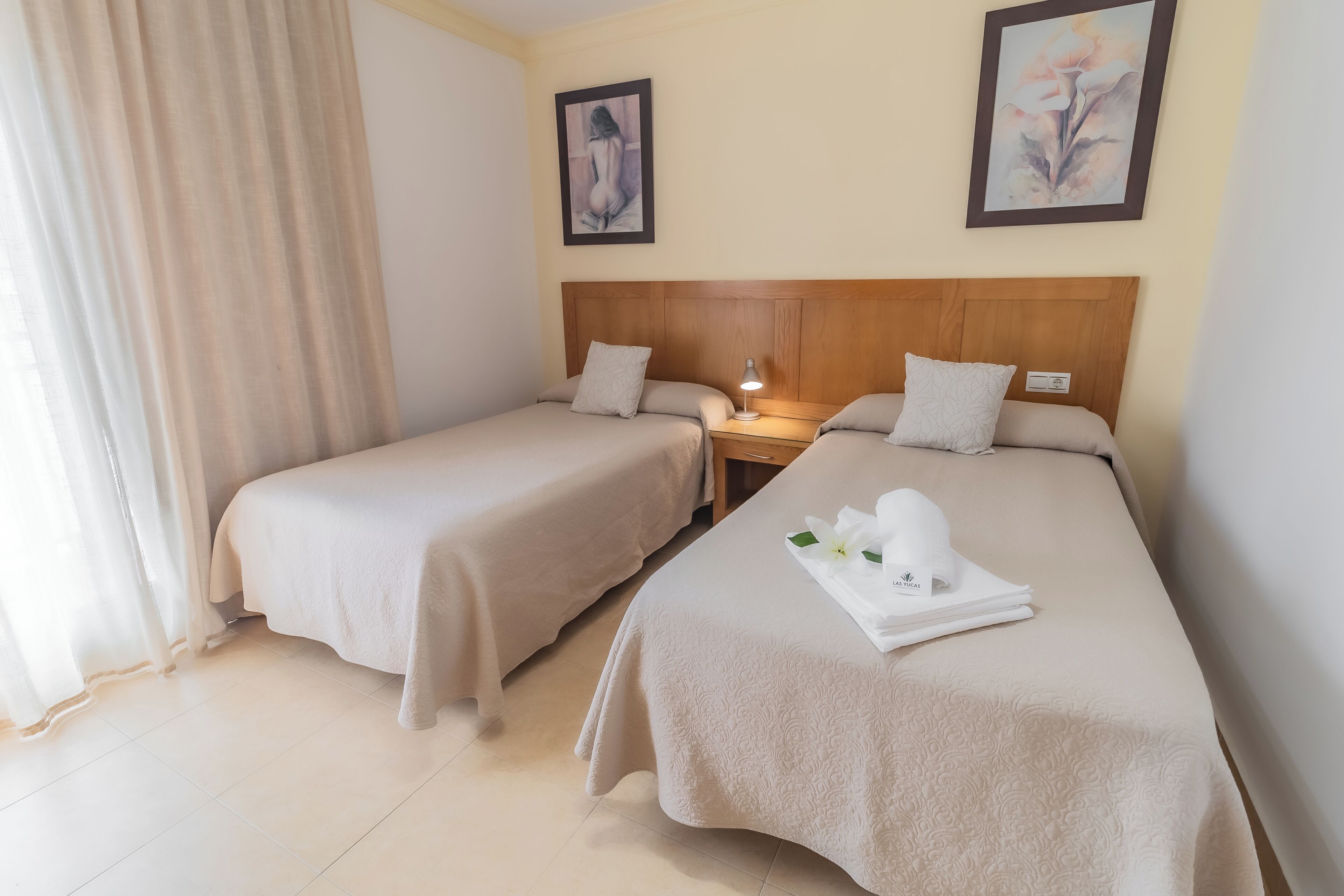 Quarto de hotel com duas camas, mesa de cabeceira e obras de arte nas paredes.