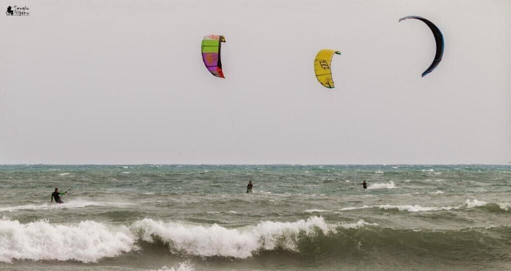 Una playa con olas y tres cometas volando en el cielo.