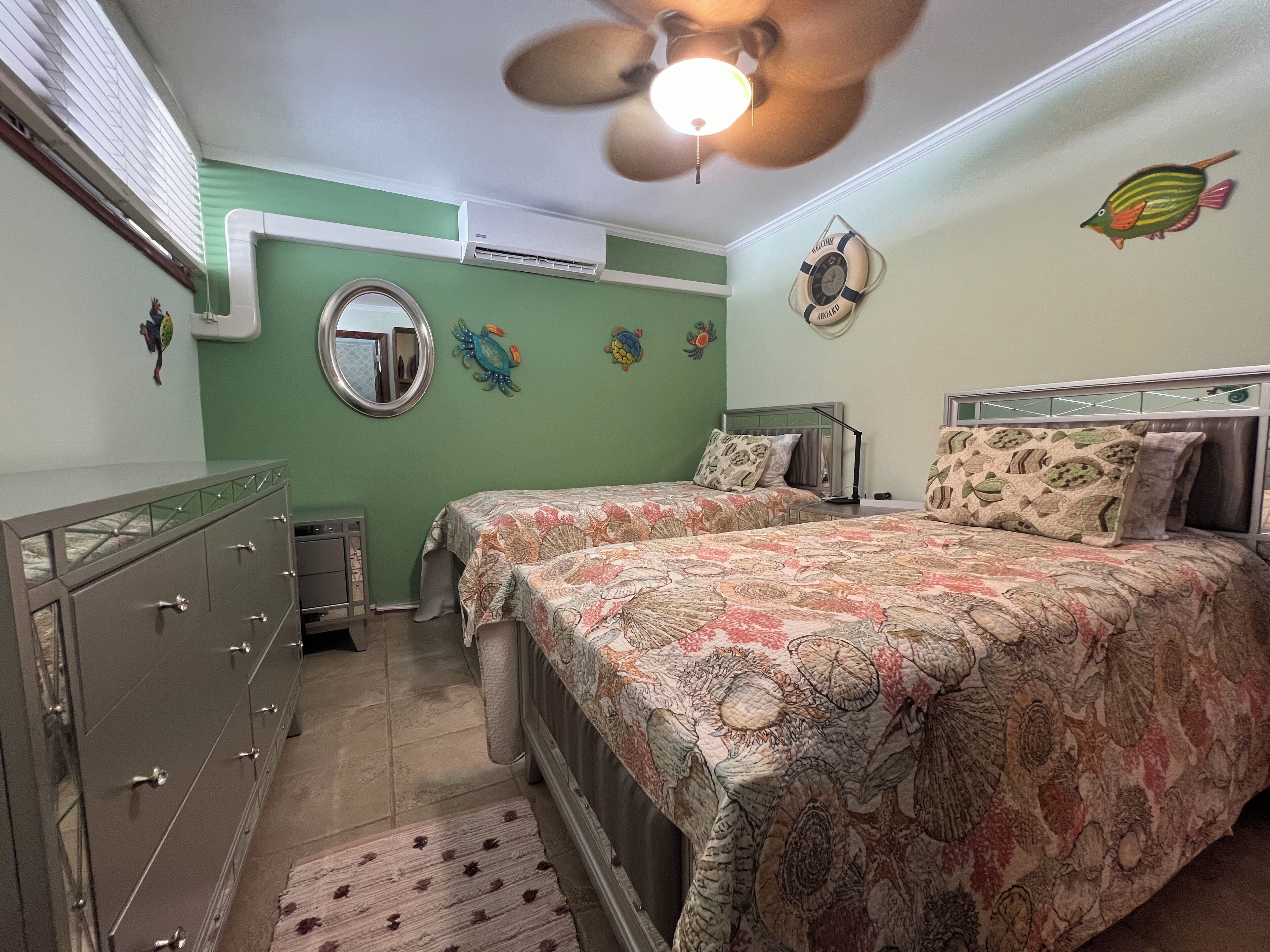 A bedroom with two beds, a dresser, a ceiling fan, and decorative wall art.