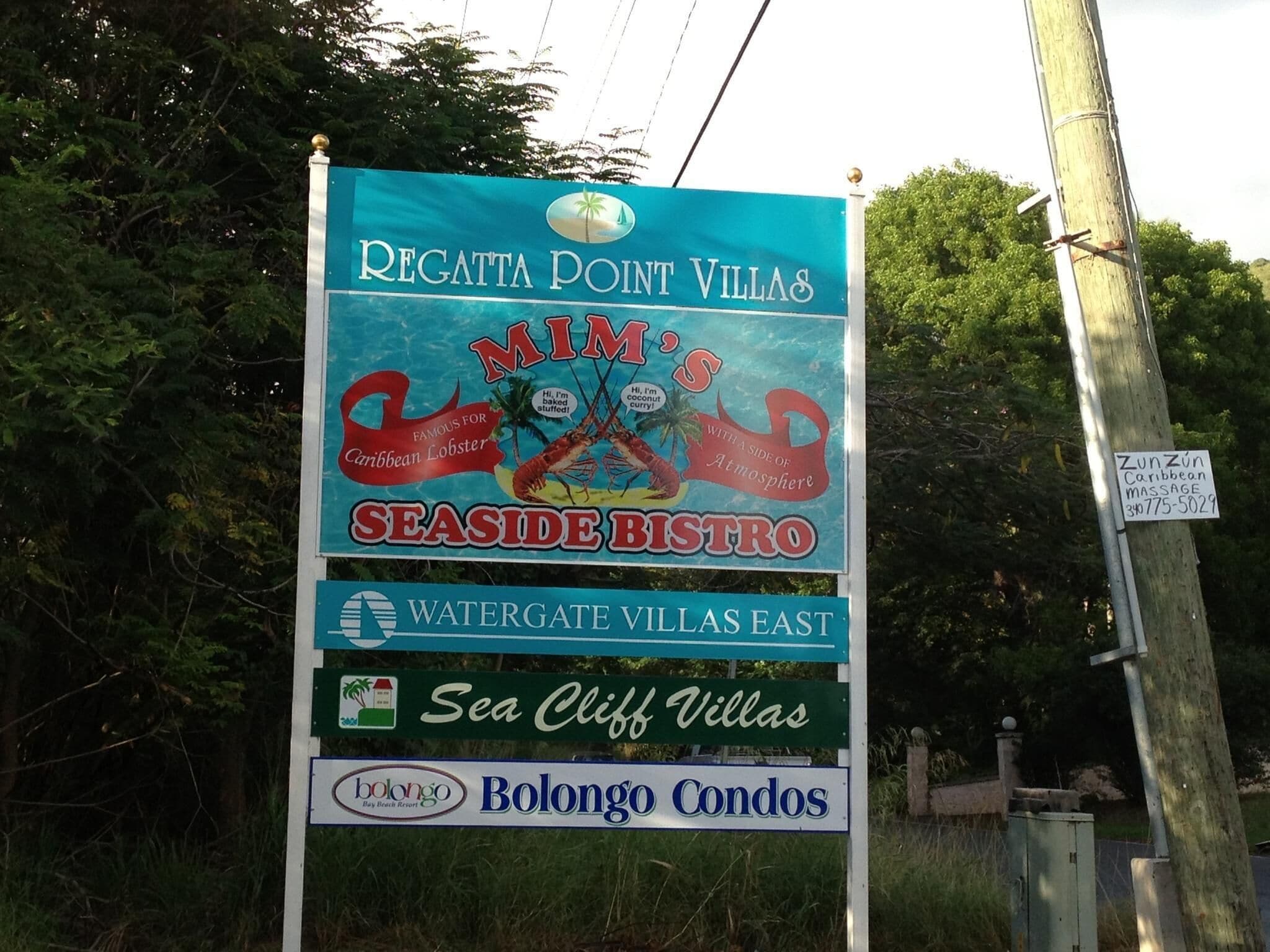 A signboard for Regatta Point Villas advertising amenities like Mimi's Seaside Bistro, Watergate Villas East, Sea Cliff Villas, and Bolongo Condos.