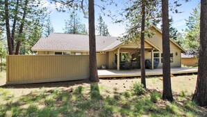 A single-story house with a covered porch, surrounded by tall trees and a wooden fence.