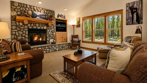 A cozy living room with a stone fireplace, a large window with a forest view, and a comfortable seating area.