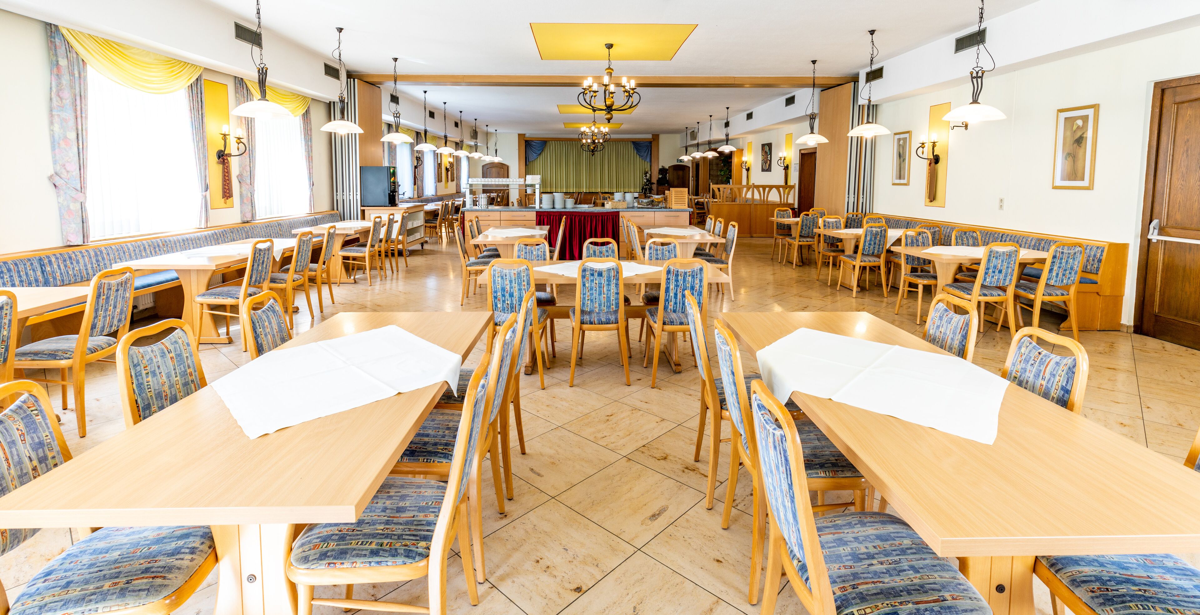 A spacious dining area with multiple tables and chairs, a central bar area, and a chandelier.