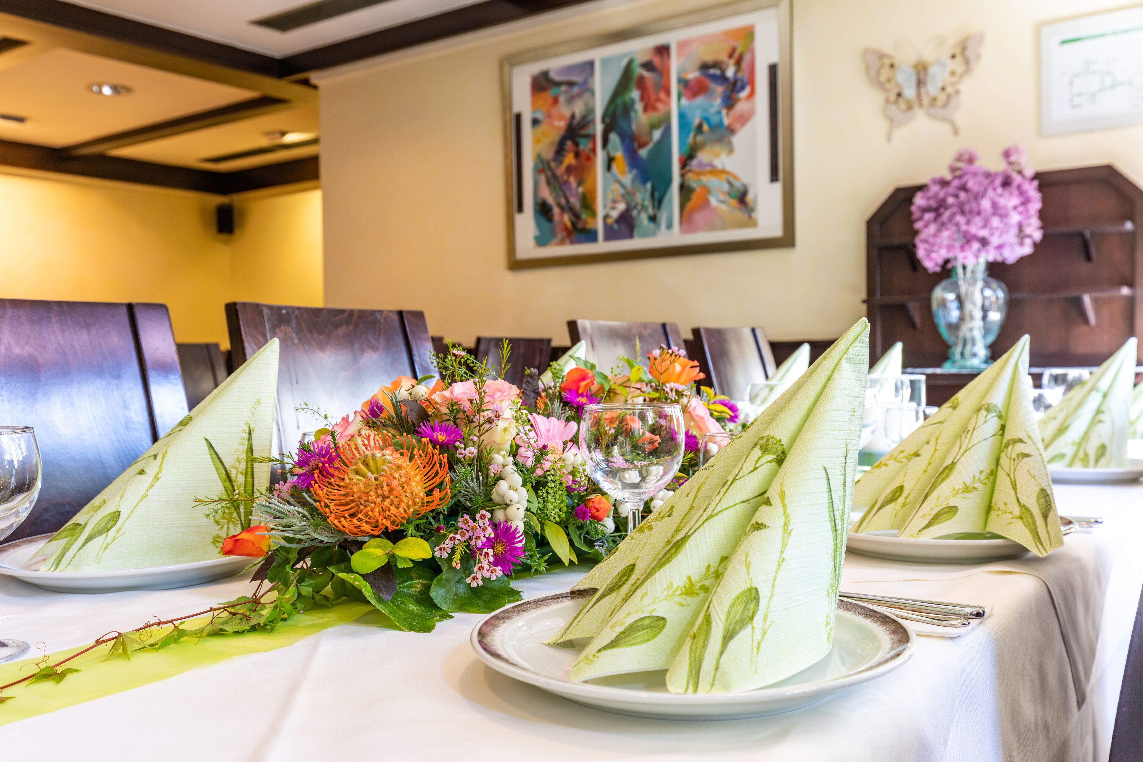 Una mesa de comedor servida con platos, servilletas y un centro de mesa floral.